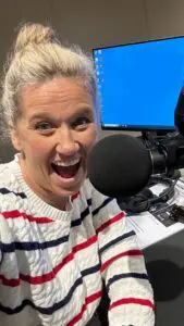 Meg Coffey taking a selfie at a radio microphone, in a striped jumper